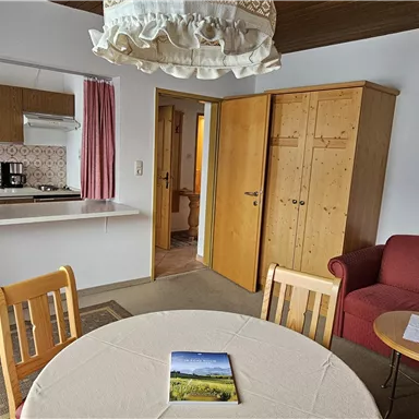 A cozy apartment with an open kitchen and a dining area. The room features a red sofa and a table with chairs.