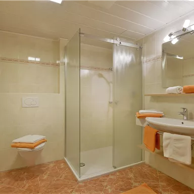 Ein modernes Badezimmer mit einer Glasdusche und einem bereitgestellten Waschbecken. Handtücher in orange und weiß sorgen für einen frischen Akzent.