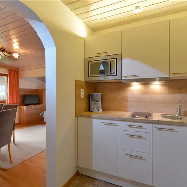 Eine moderne Küchenzeile mit hellen Schränken und einem Holzrückwand. Im Hintergrund ist ein Essbereich mit Tisch und Stühlen zu sehen.