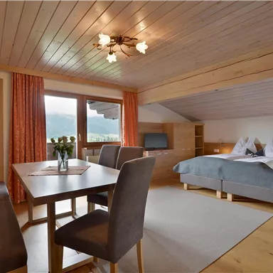 Ein gemütliches Zimmer mit Doppelbett und einem Esstisch. Große Fenster lassen viel Licht herein und bieten einen schönen Blick auf die Umgebung.
