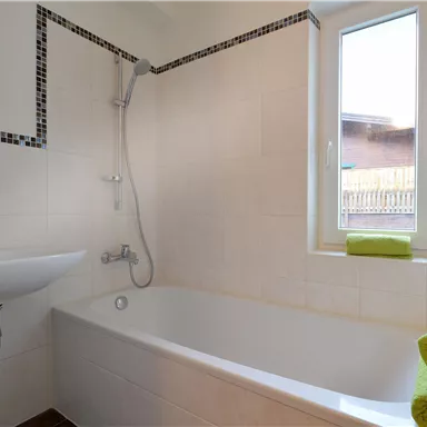 Ein modernes Badezimmer mit einer Badewanne und einer Dusche. Das Fenster sorgt für natürliches Licht, und grüne Handtücher verleihen einen frischen Akzent.