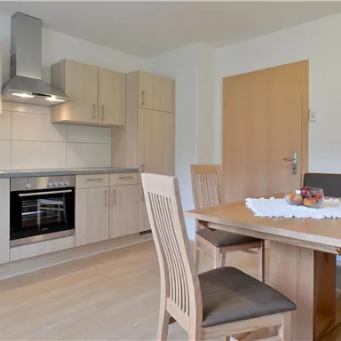 Eine moderne Küche mit Holzschränken und einem Essbereich. Der Raum ist hell und freundlich eingerichtet.