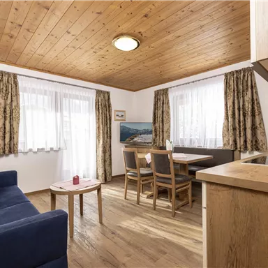 Ein gemütlicher Wohnraum mit einer blauen Couch und einem Holztisch. Große Fenster sorgen für viel Tageslicht und eine einladende Atmosphäre.