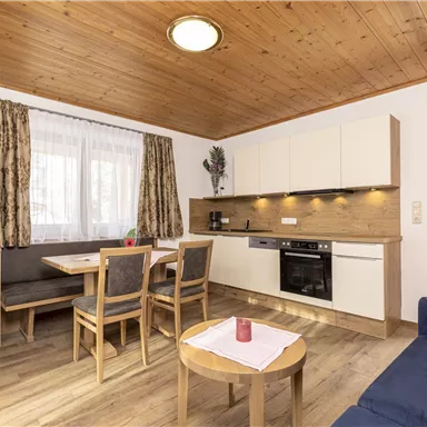 Eine gemütliche Wohnküche mit Holzdecken und modernen Möbeln. Der Raum ist hell und einladend, mit einem Esstisch und einer Sitzgelegenheit.