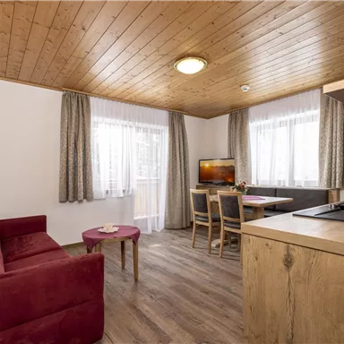 Eine gemütliche Wohnküche mit einem Sofa und einem Tisch. Große Fenster lassen viel Licht herein und sorgen für eine einladende Atmosphäre.