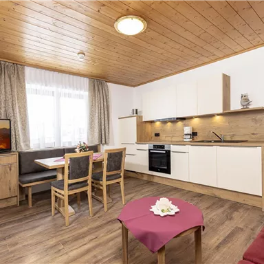 Eine moderne Küche mit Holzdekor und einem Essbereich. Das Zimmer hat einen Fernseher, helle Vorhänge und ein gemütliches Ambiente.