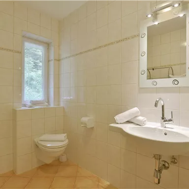A modern bathroom with bright tiles and a large mirror. There is a shower, a sink, and a toilet.