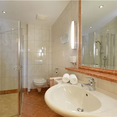 Ein modernes Badezimmer mit einer Dusche und einem Waschbecken. Die Wände sind hell gefliest und es gibt große Spiegel.