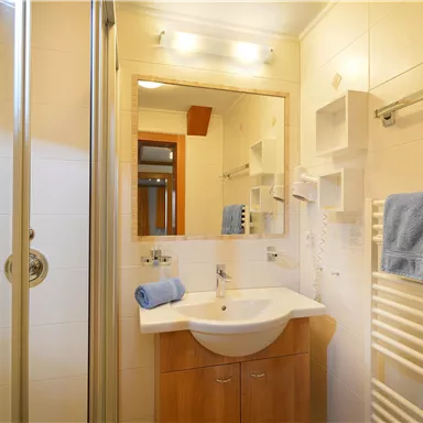 Ein helles Badezimmer mit Dusche und Waschbecken. Handtücher und ein Spiegel sind ebenfalls vorhanden.