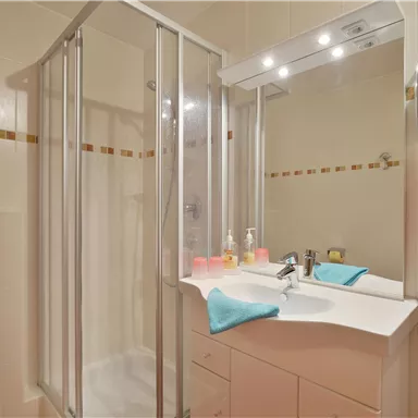 Ein modernes Badezimmer mit einer Duschkabine und einem Waschbecken. Die Wände sind hell und es gibt farbige Handtücher für einen frischen Akzent.