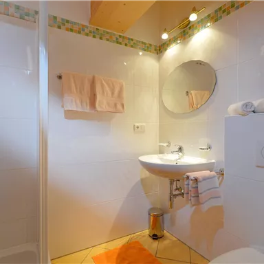 Ein modernes Badezimmer mit einer Dusche, einem Waschbecken und einem großen Spiegel. Die Wände sind hell gefliest und das Ambiente wirkt sauber und einladend.