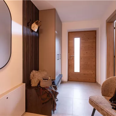A modern hallway with a round mirror, a wooden barn door, and a stylish armchair. The walls are bright, and the space feels inviting and cozy.