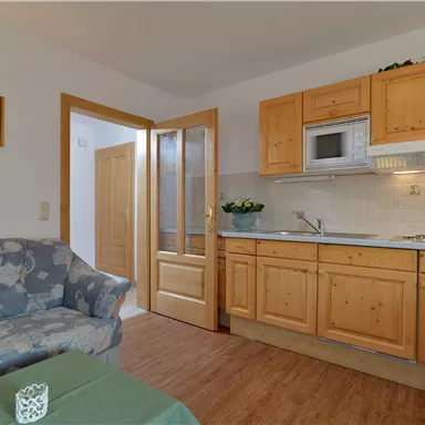 Eine gemütliche Wohnküche mit Holzschränken und modernen Geräten. Der Raum ist hell und einladend, mit einem Sofa und einem Tisch.