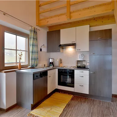 Eine moderne Küche mit Holzregalen und hellen Schränken. Große Fenster sorgen für viel Tageslicht.