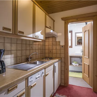 Eine kleine Küche mit hellen Holzschränken und moderner Ausstattung. Der Raum ist ordentlich und einladend mit einem Zugang zu einem weiteren Raum.