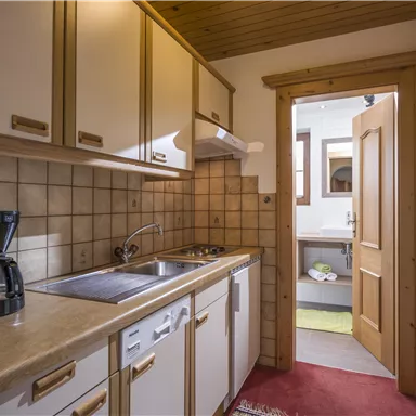 Eine kleine Küche mit hellen Holzschränken und moderner Ausstattung. Der Raum ist ordentlich und einladend mit einem Zugang zu einem weiteren Raum.