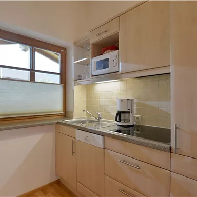 Eine helle Küche mit Holzschränken und modernen Geräten. Ein Fenster sorgt für Tageslicht und eine freundliche Atmosphäre.