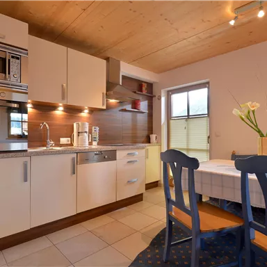 A modern kitchen with bright cabinets and a spacious countertop. There are flowers in a vase on the table and various kitchen appliances.
