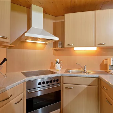 Eine moderne Küche mit hellen Holzschränken und einem Herd. Die Arbeitsfläche ist gut organisiert und es gibt eine Spüle sowie eine Küchenmaschine.