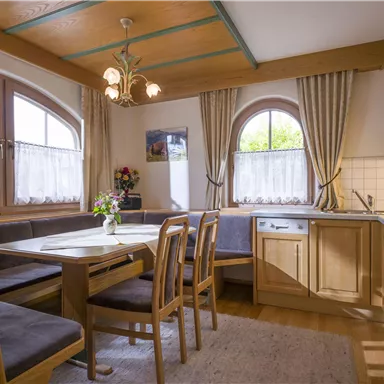 Eine gemütliche Küche mit Holzmöbeln und einem Essbereich. Große Fenster lassen viel Licht herein und schaffen eine einladende Atmosphäre.