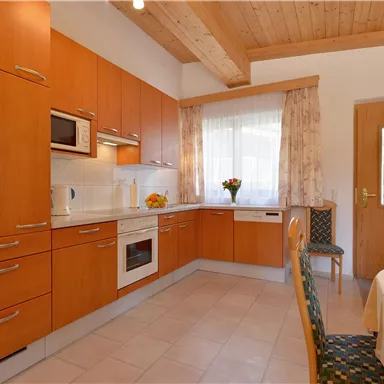 Eine moderne Küche mit Holzschränken und hellen Wänden. Es gibt einen Tisch mit Stühlen und frischen Blumen auf der Arbeitsplatte.