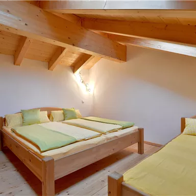 Ein helles, gemütliches Schlafzimmer mit Holzdecke und zwei Betten. Die Betten sind mit gelben Bettlaken und Kissen dekoriert.
