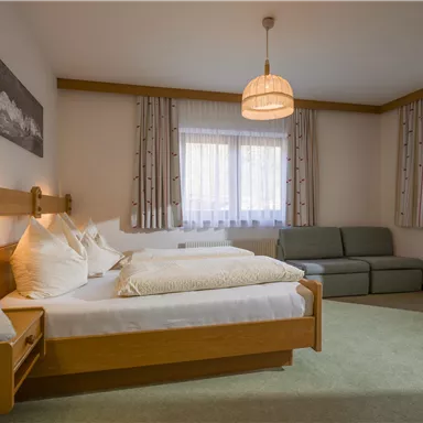 Ein gemütliches Schlafzimmer mit zwei Betten und einem Sofa. Die Fenster lassen viel Licht herein und die Einrichtung ist schlicht und modern.