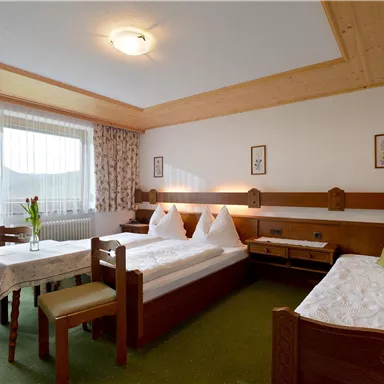 A cozy hotel room with two beds and a table. Large windows let in plenty of light and the space is decorated with natural materials.