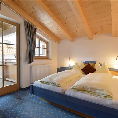 A cozy bedroom with wooden ceilings and a large double bed. The room has a balcony with an outdoor view.