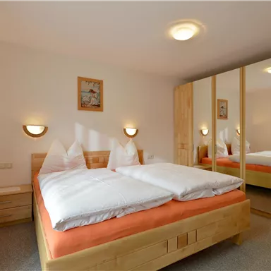 Ein gemütliches Schlafzimmer mit einem großen Doppelbett und hellen Holzmöbeln. Die Wände sind in sanften Farben gehalten, und ein Spiegel sorgt für mehr Licht im Raum.