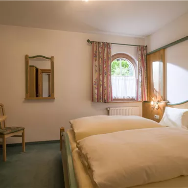 Ein gemütliches Schlafzimmer mit einem großen Bett und einem Tisch. Die Fenster lassen viel natürliches Licht herein und die Wände sind hell und freundlich.