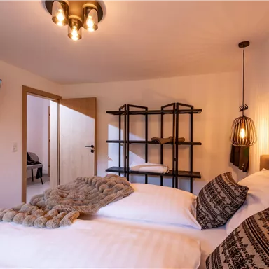A cozy bedroom with two beds and a modern design. A television is mounted on the wall, and there is a decorative shelving area.