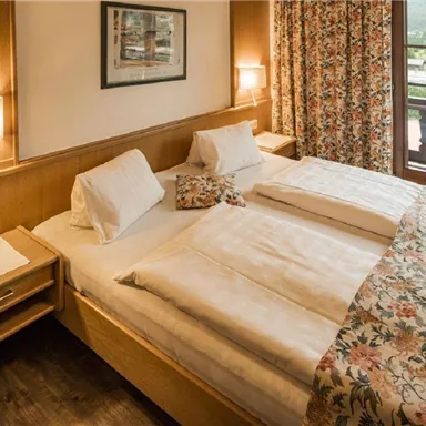 A cozy hotel room with two beds and wood paneling. Large windows offer a view of the countryside and let in plenty of daylight.