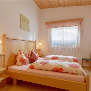 Ein gemütliches Schlafzimmer mit zwei Betten und hellen Farben. Große Fenster sorgen für viel Tageslicht und eine einladende Atmosphäre.