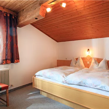 Ein gemütliches Schlafzimmer mit einem Doppelbett und einem Stuhl. Die Wände sind mit Holz verkleidet und das Fenster lässt viel Tageslicht herein.
