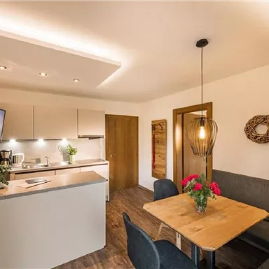 A modern kitchen with a dining area and a cozy sofa. Plants and decorations create an inviting atmosphere.