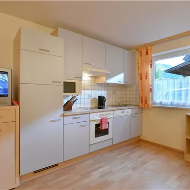 Eine moderne Küche mit hellen Möbeln und Holzfußboden. Fenster mit Vorhängen lassen natürliches Licht herein.