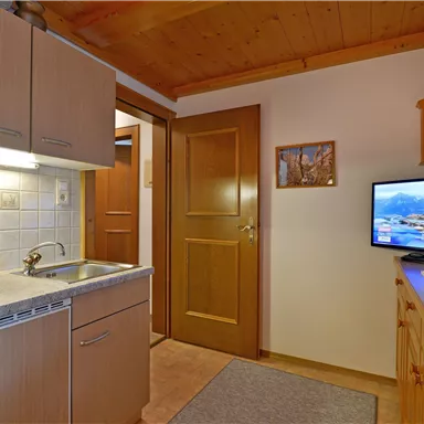 A cozy kitchen nook with modern appliances and wooden paneling. A television is also visible, along with an open door to another room.