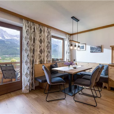An inviting dining area with a table and chairs, surrounded by large windows overlooking the mountains. The decor is modern and cozy, featuring warm wood tones and a pleasant atmosphere.
