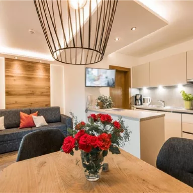 A modern and cozy kitchen dining area with a dining space. On the table is a vase with red roses, and the furniture is in warm, neutral colors.