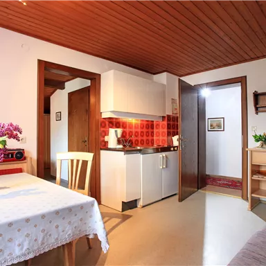 Eine gemütliche Wohnung mit einer kleinen Küche und einem Essbereich. Auf dem Tisch steht eine Vase mit bunten Blumen.