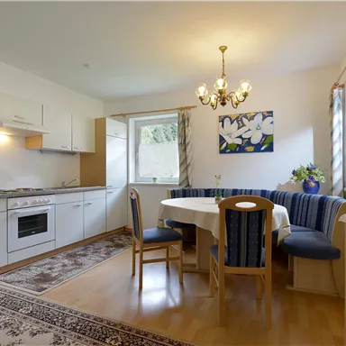 A bright kitchen with modern furniture and a dining area. The room is designed in a friendly manner and has large windows for daylight.