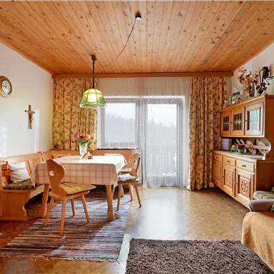 A cozy living space with a wooden ceiling and a dining table. The furnishings include a television, a sofa, and decorative furniture.