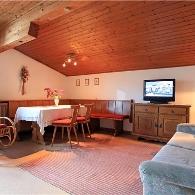 Ein gemütliches Wohnzimmer mit einem Holzdecken und einem Teppich. Es gibt ein Esszimmer, eine Couch und einen Fernseher.