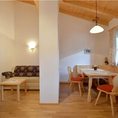 Ein gemütlicher Wohnbereich mit Holzdecke und Tischgruppe. Ein Sofa und Stühle schaffen eine einladende Atmosphäre.