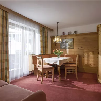 Ein gemütlicher Wohnraum mit Holzmöbeln und einem Esstisch. Große Fenster lassen viel Licht herein und bieten einen einladenden Blick.