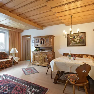 Ein gemütliches Wohnzimmer mit Holzdecke und rustikalen Möbeln. Ein runder Tisch und eine elegante Dekoration schaffen eine einladende Atmosphäre.