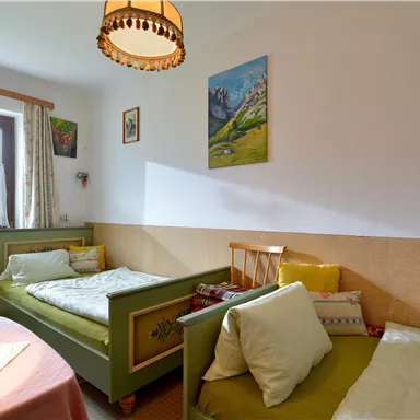 A cozy room with two single beds and a small table. The walls are decorated with pictures and decorative elements.