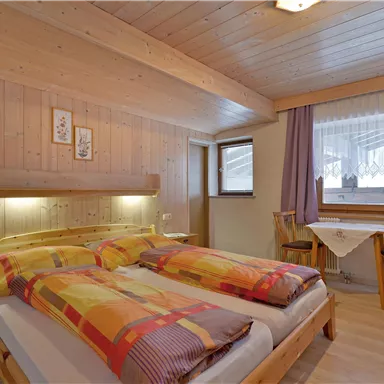 Ein gemütliches Schlafzimmer mit Holzwänden und einem Doppelbett. Es gibt zwei Fenster, die viel Licht hereinlassen, sowie eine kleine Sitzecke.