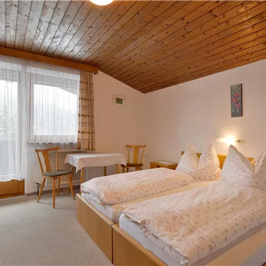 Ein gemütliches Schlafzimmer mit zwei getrennten Betten und Holzverkleidung. Große Fenster lassen viel Licht herein und bieten einen Blick auf die Außenansicht.